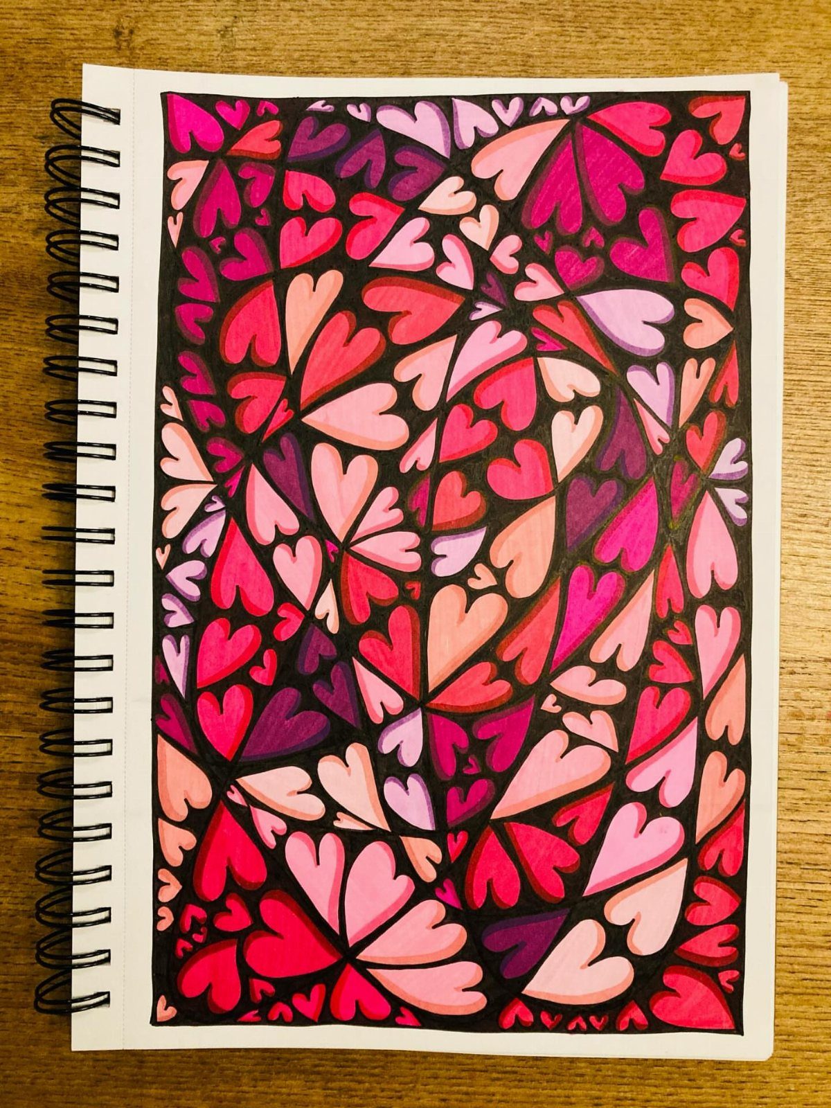 Spiral pattern of pink and red hearts colored in a spiral sketchbook