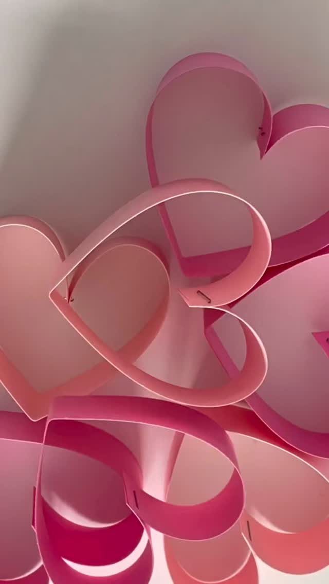 Pink and magenta 3D cardstock hearts attached to a white wall.
