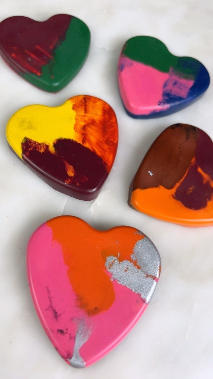 Heart-shaped crayons in colorful swirls resting on a white marble surface.