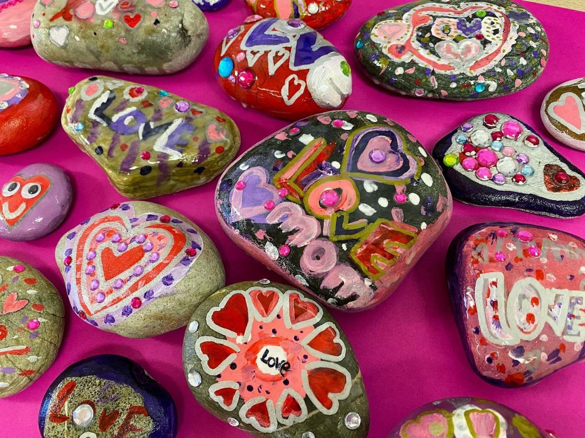 Painted rocks with colorful hearts and love messages on a pink background