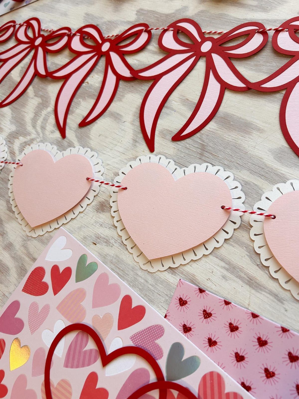 Red bow and pink heart paper garlands on a light wooden surface.