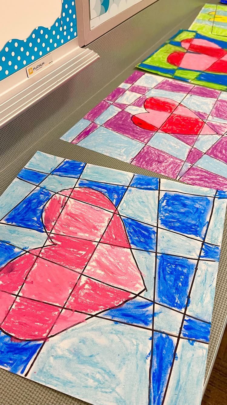 Children's heart drawings with colorful grid backgrounds laid out on a grey table.