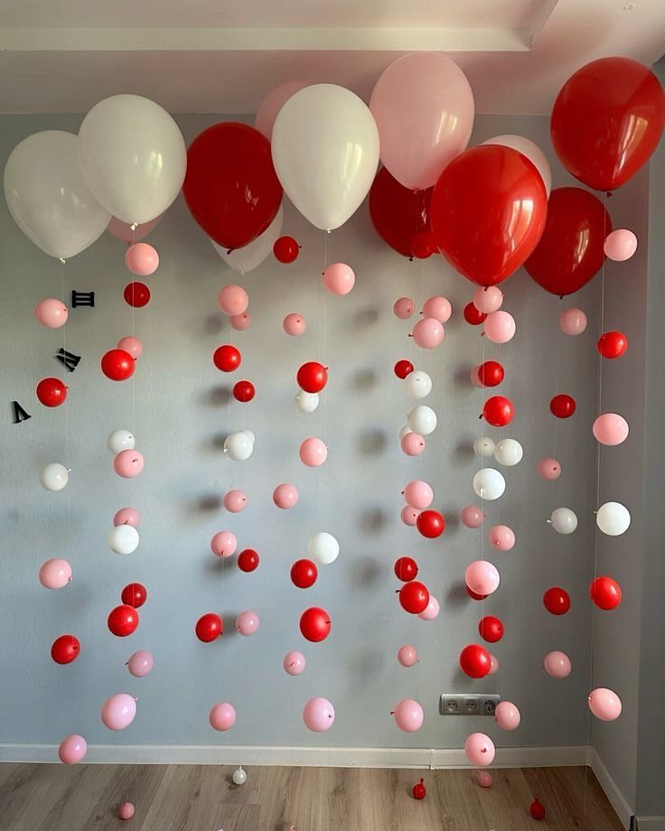 Red, white, and pink balloons hanging from a ceiling against a grey wall.