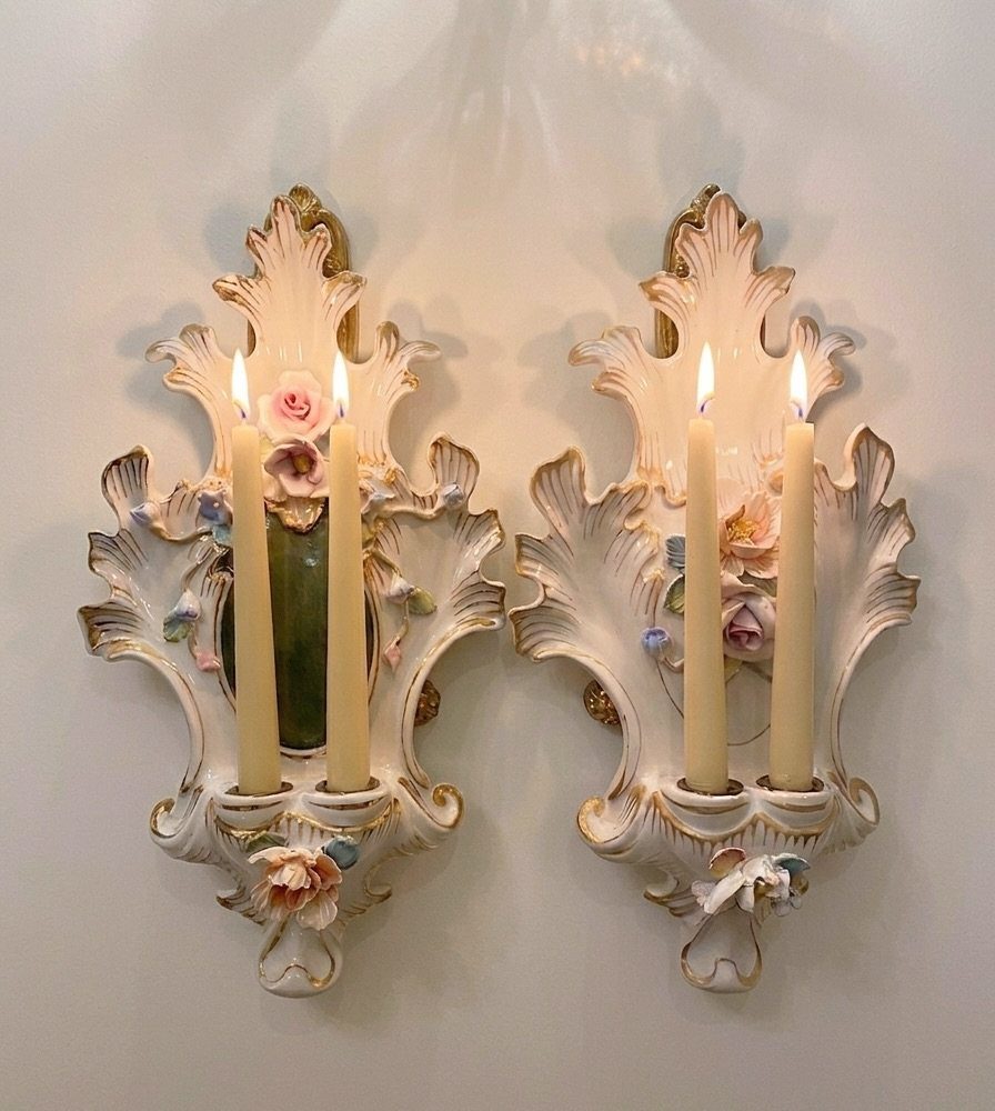 Ornate white ceramic wall candle holders with lit taper candles and floral details.