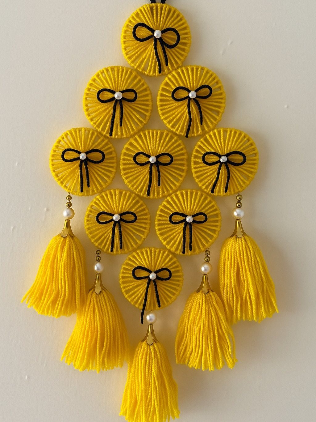 Yellow circular wall hanging with black bows and long yellow tassels on white wall