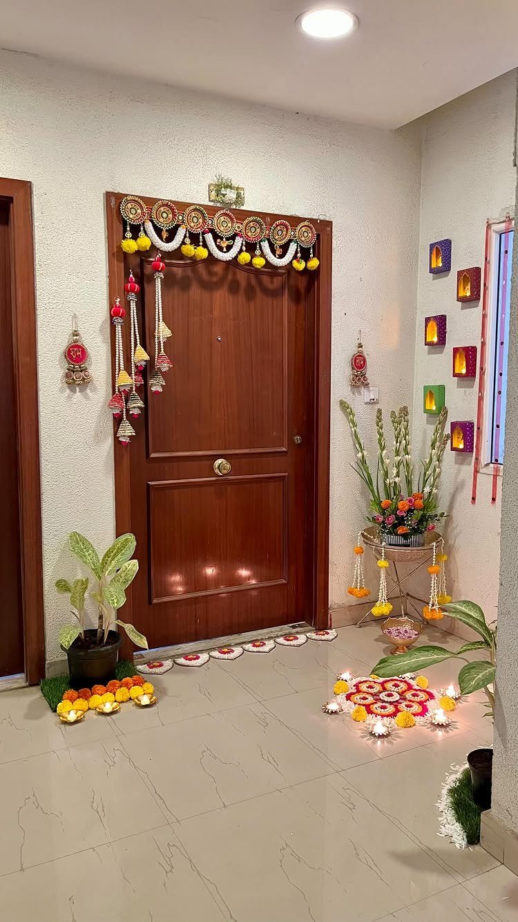 Wooden door decorated with a traditional yellow floral toran and floor rangoli.