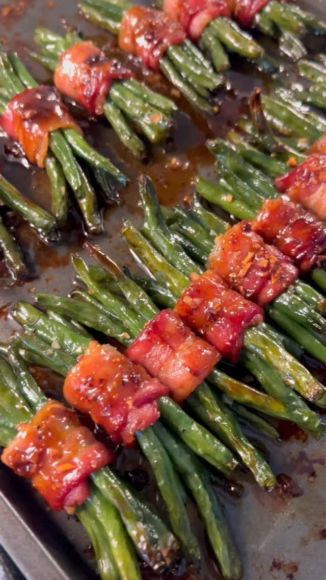 Green bean bundles wrapped in glazed bacon on a dark baking sheet.