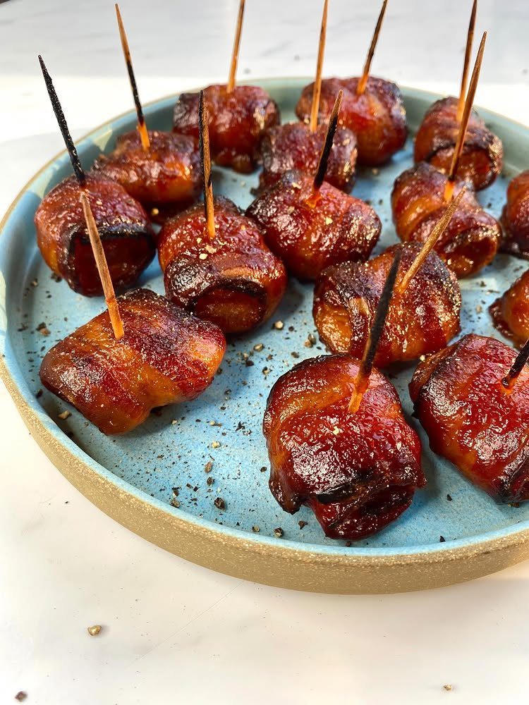 Bacon-wrapped water chestnuts on toothpicks served on a light blue ceramic plate.