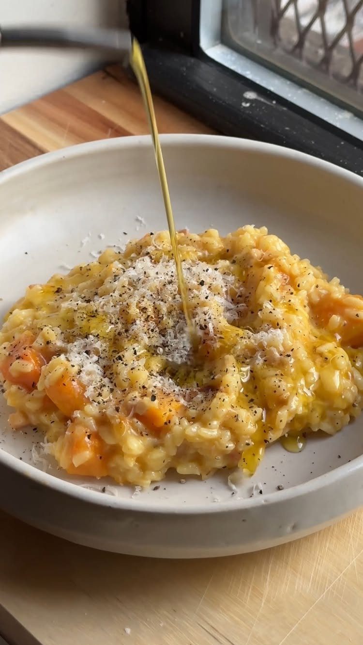 Butternut squash risotto in a white bowl with oil being poured over top.