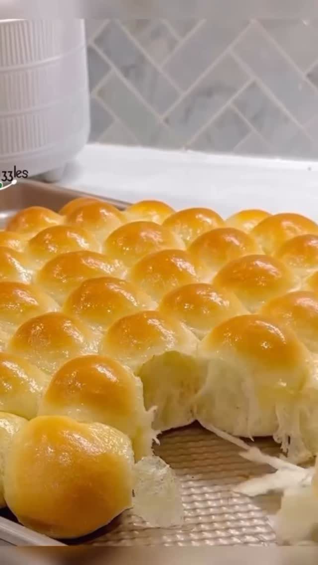 Golden-brown glossy pull-apart dinner rolls on a baking sheet in a kitchen.