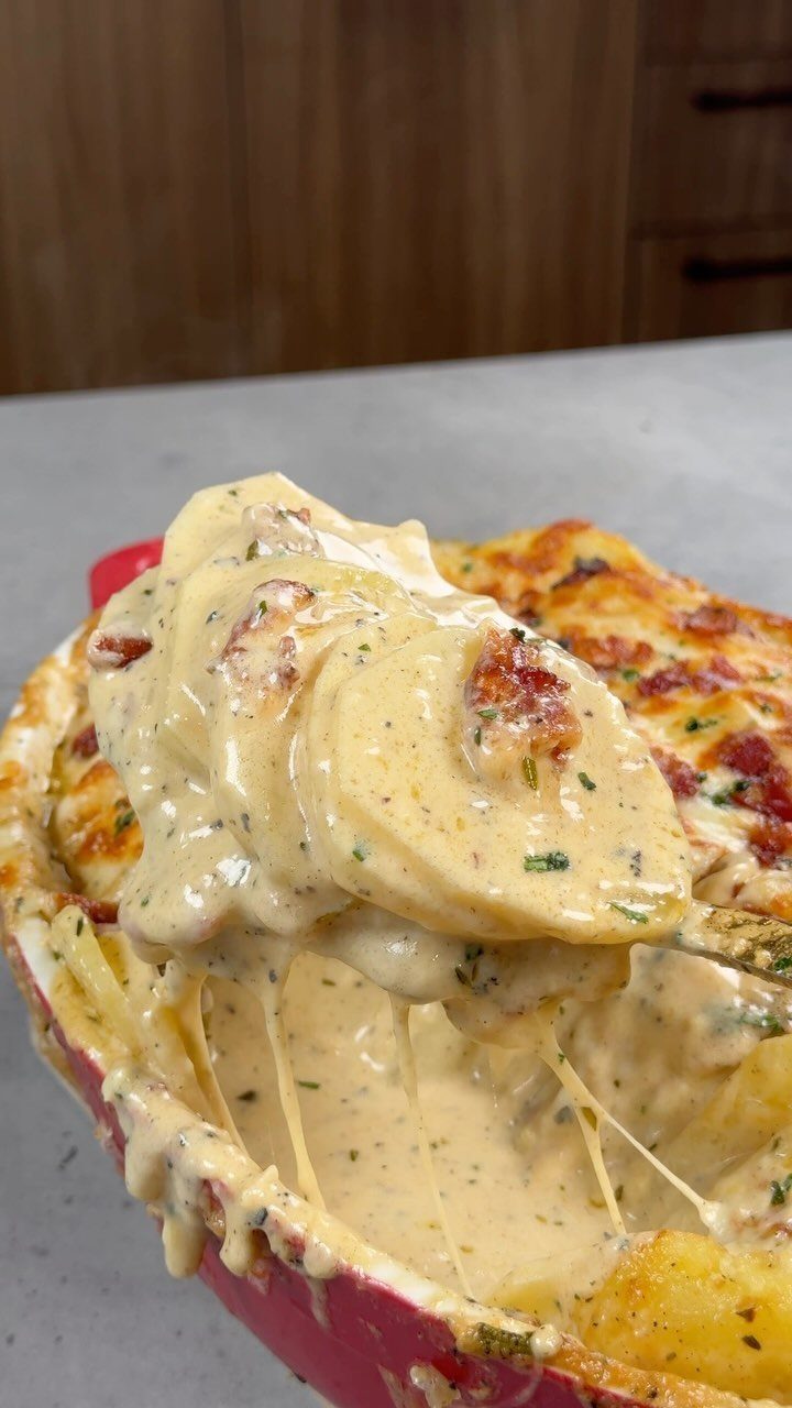 Cheesy scalloped potatoes with creamy sauce in a red ceramic baking dish.