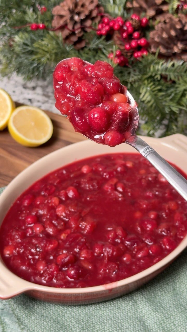 Cranberry sauce in a ceramic dish with a spoonful lifted upward.