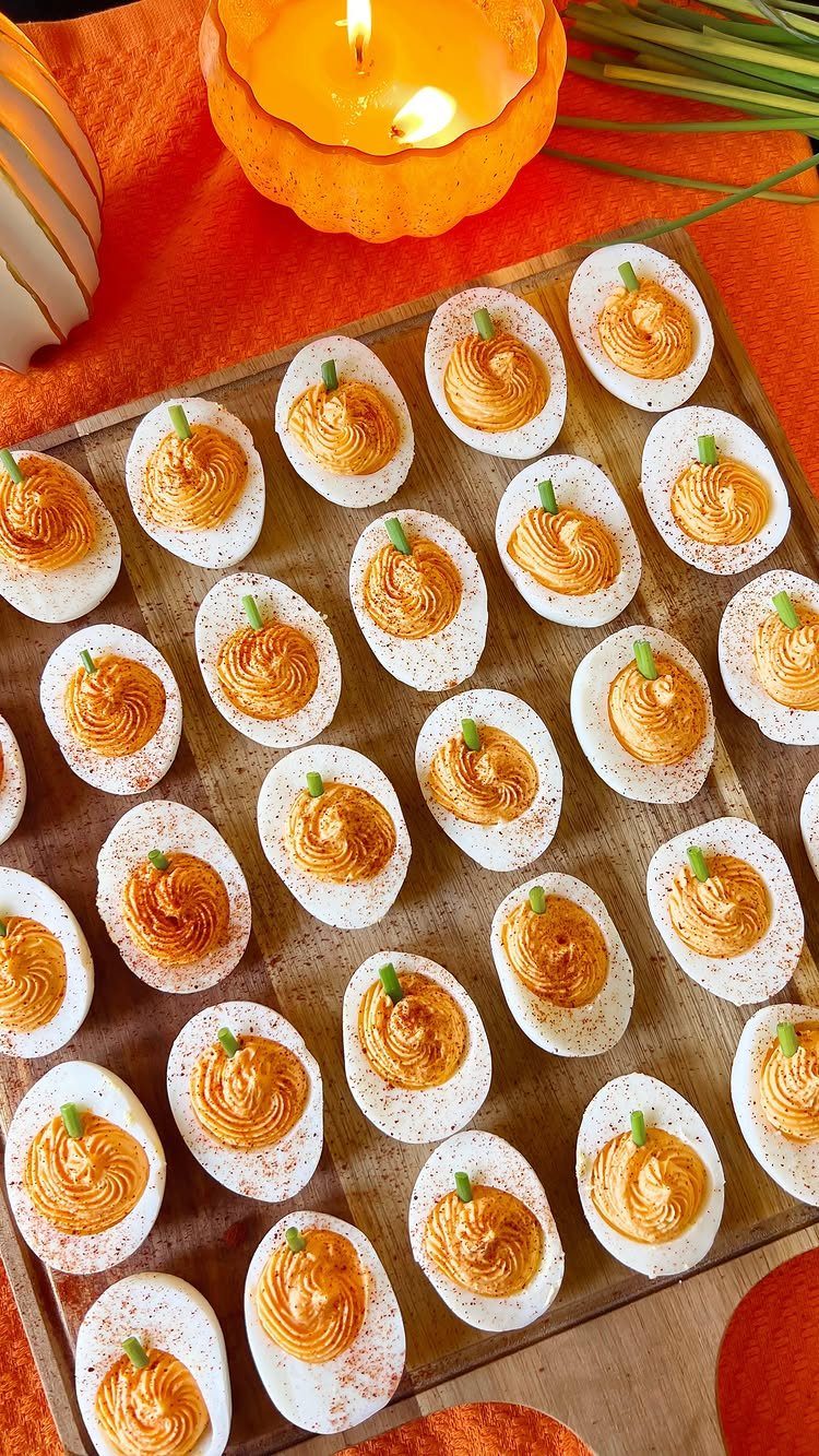 Deviled eggs with orange pumpkin-shaped filling arranged on a wooden serving platter.