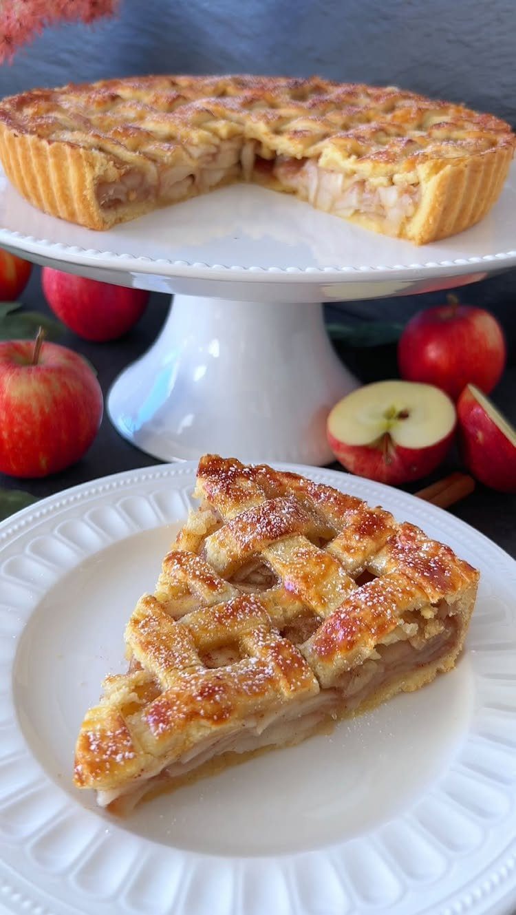 Apple tart slice with lattice crust on a white plate with red apples.