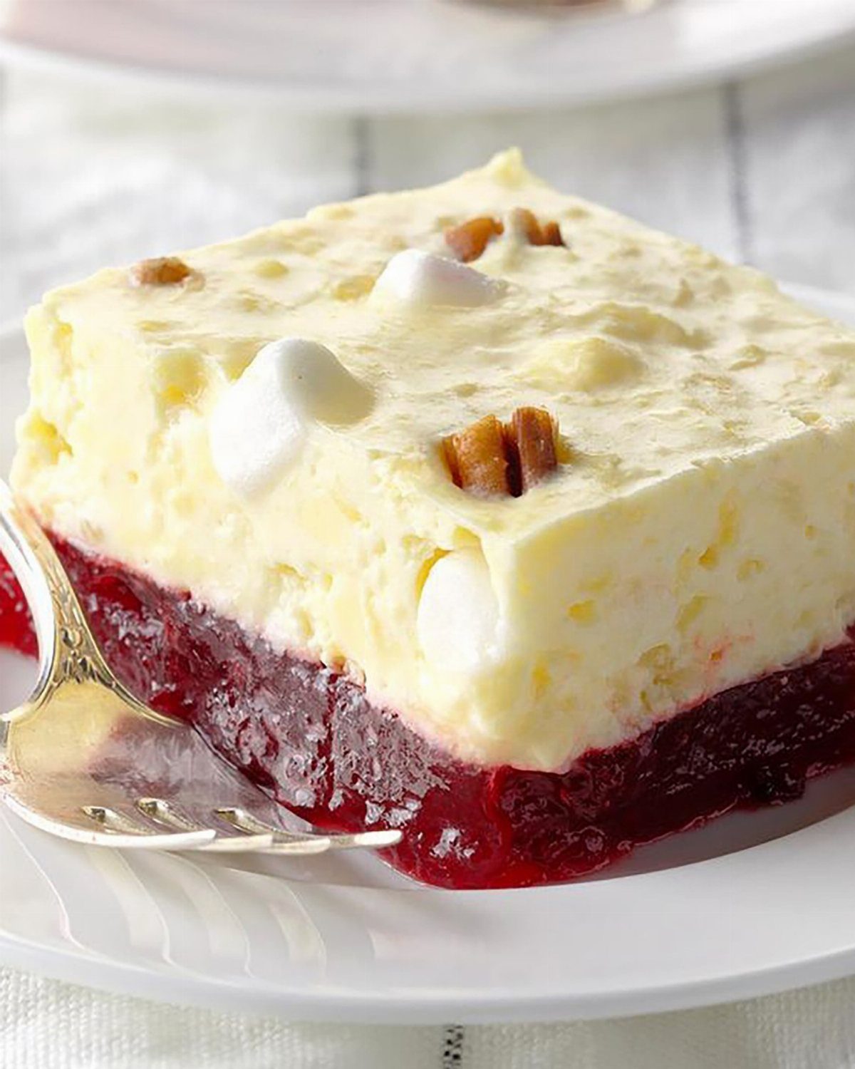 Layered dessert with red gelatin base and creamy topping with marshmallows and pecans.