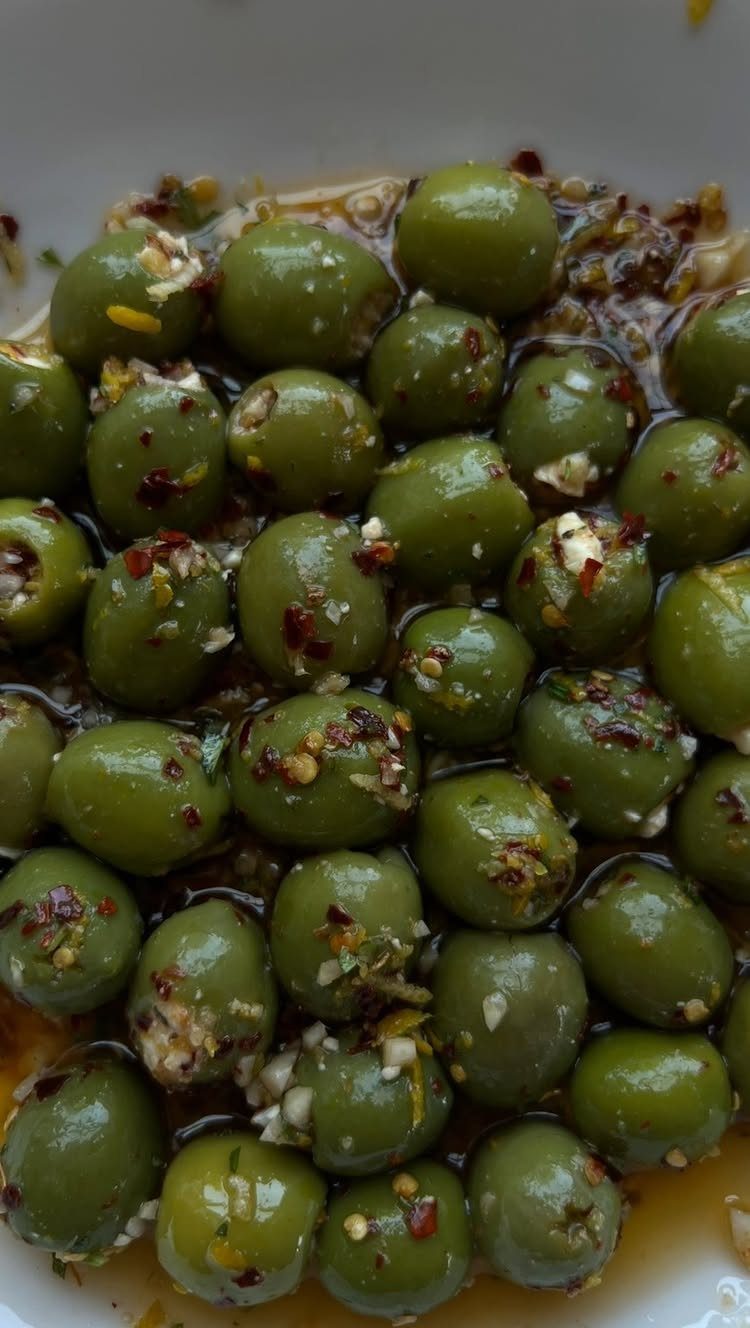 Marinated green olives with garlic and red pepper flakes in a white bowl.