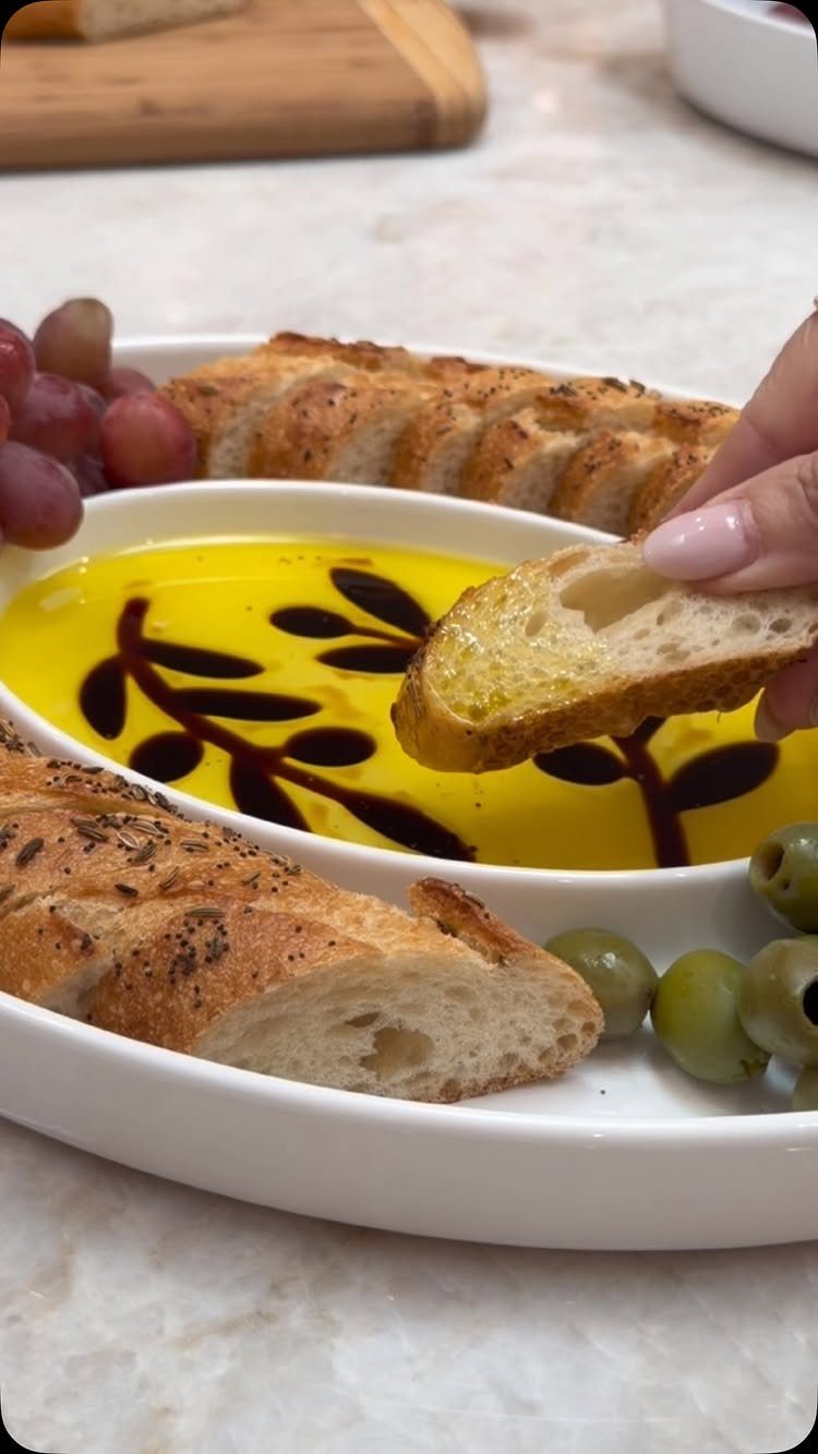 Toasted baguette slice being dipped into olive oil with balsamic glaze art.