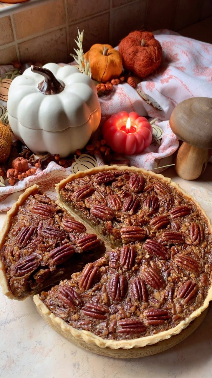 Pecan pie with a slice removed, surrounded by autumn pumpkins and a candle.