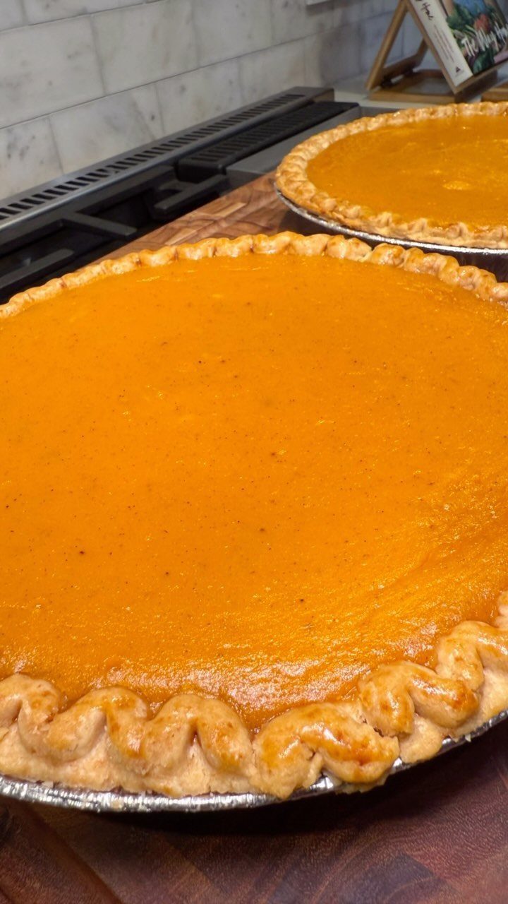 Two whole pumpkin pies with orange filling and crimped crusts on wooden surface.
