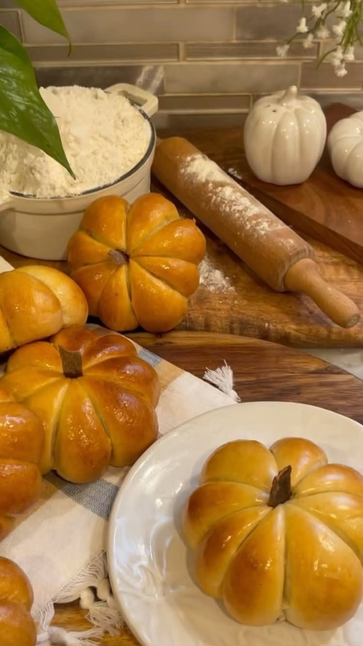 Pumpkin shaped bread rolls on a wooden board with flour and rolling pin.