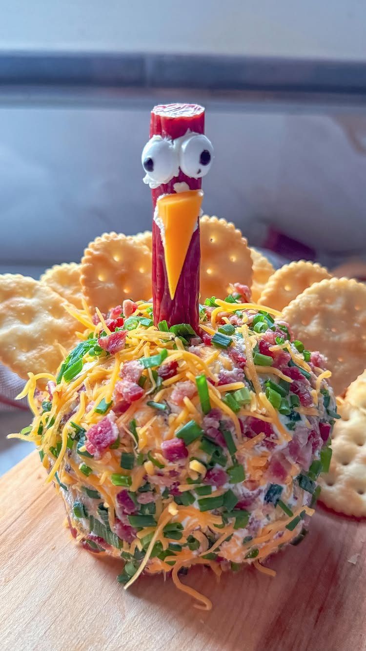Turkey-shaped cheese ball with shredded cheese and bacon, surrounded by round crackers.
