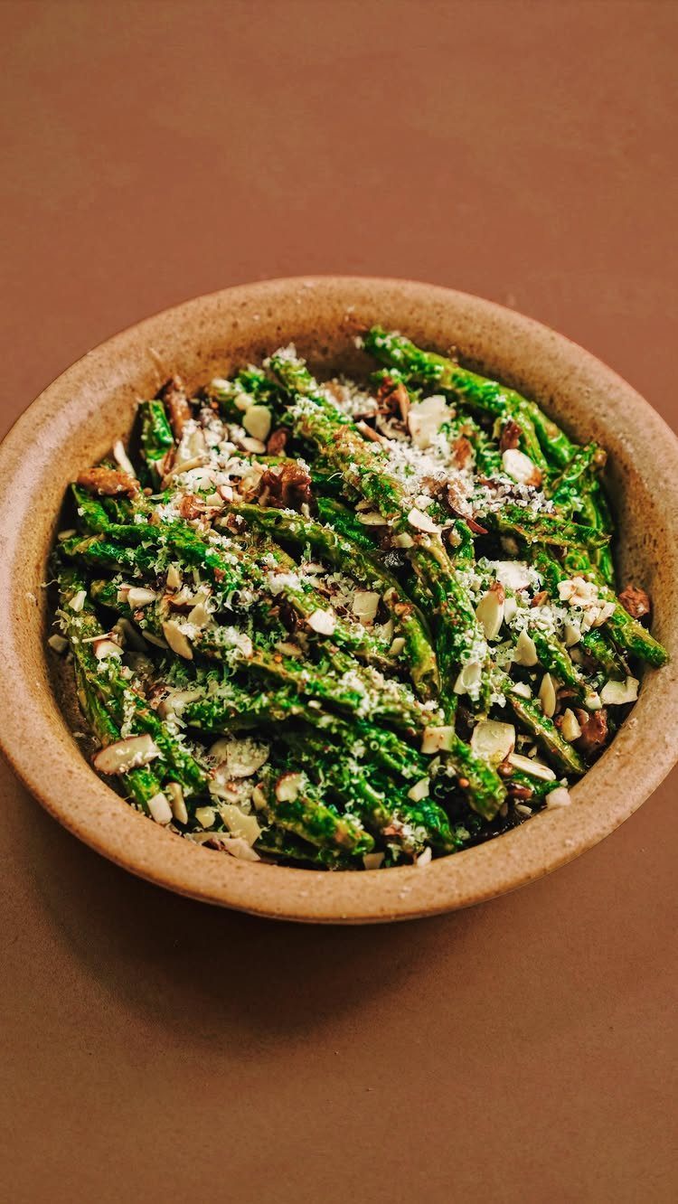 Roasted asparagus spears with slivered almonds and cheese in a tan ceramic bowl.