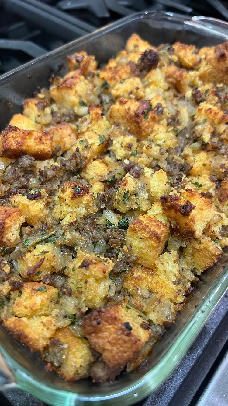 Stuffing with bread cubes and sausage in a glass baking dish on a stove.