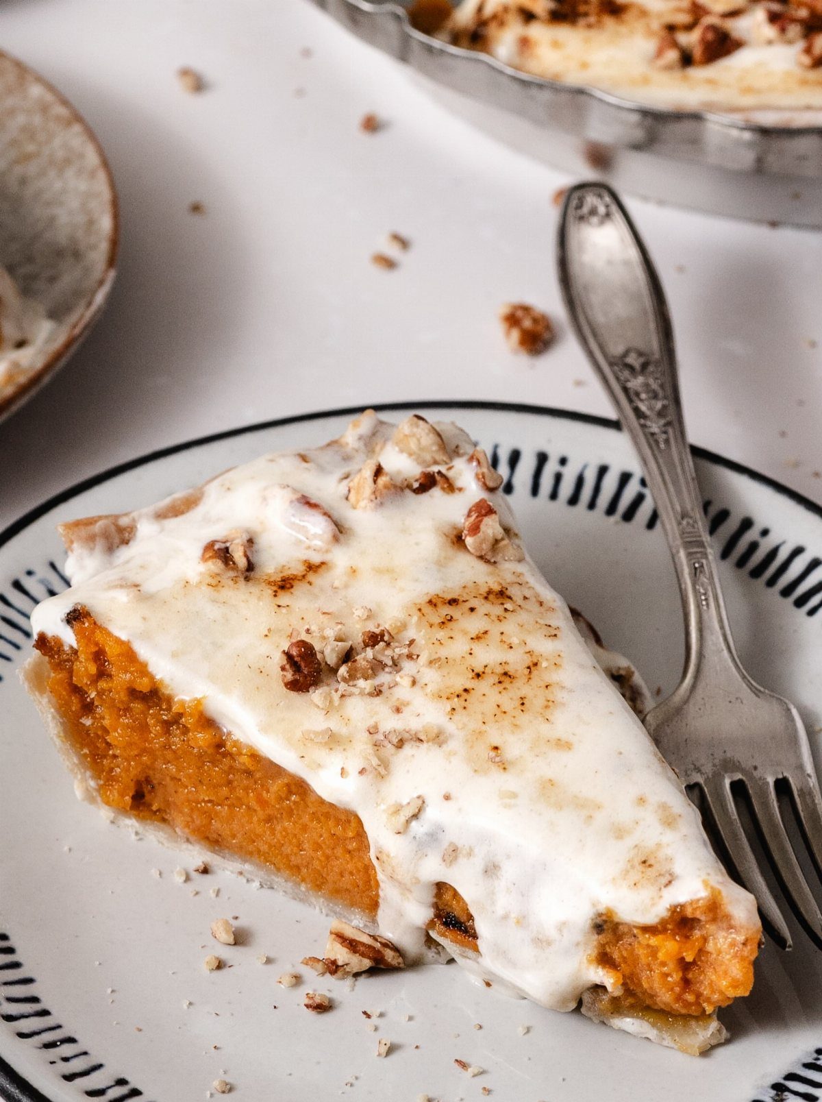 Slice of sweet potato pie topped with cream and pecans on a plate.