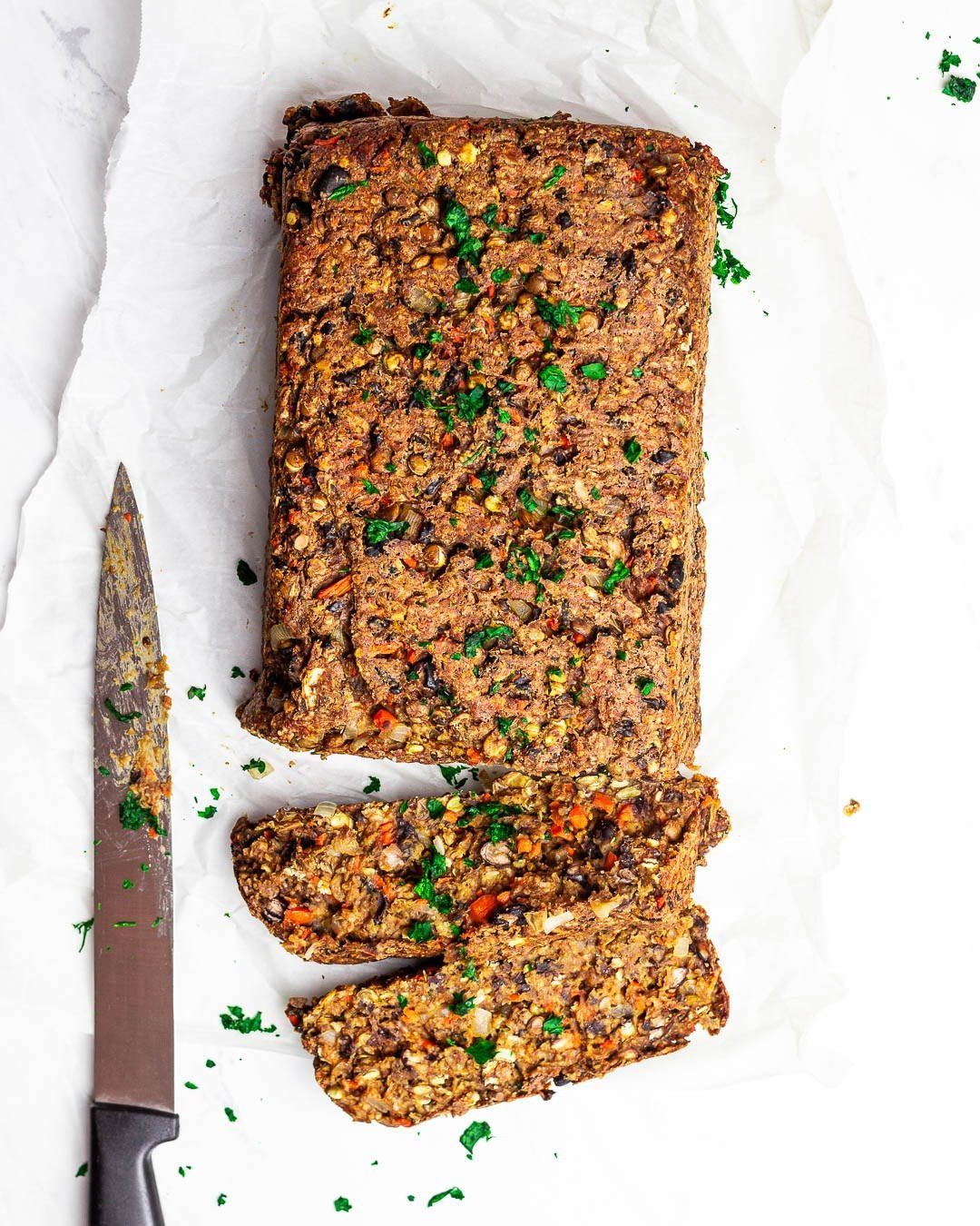 Vegetarian meatloaf with parsley on white parchment paper with two sliced pieces.