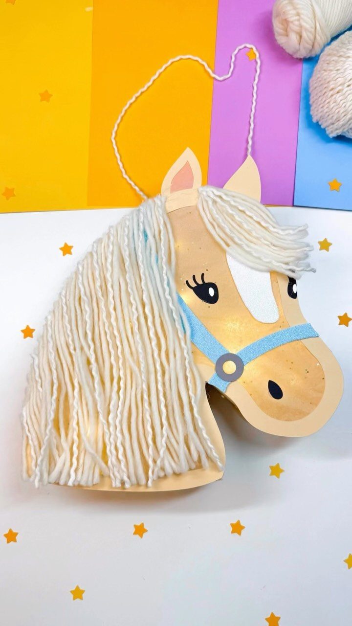 Handmade cardboard horse head craft with white yarn mane and blue bridle.