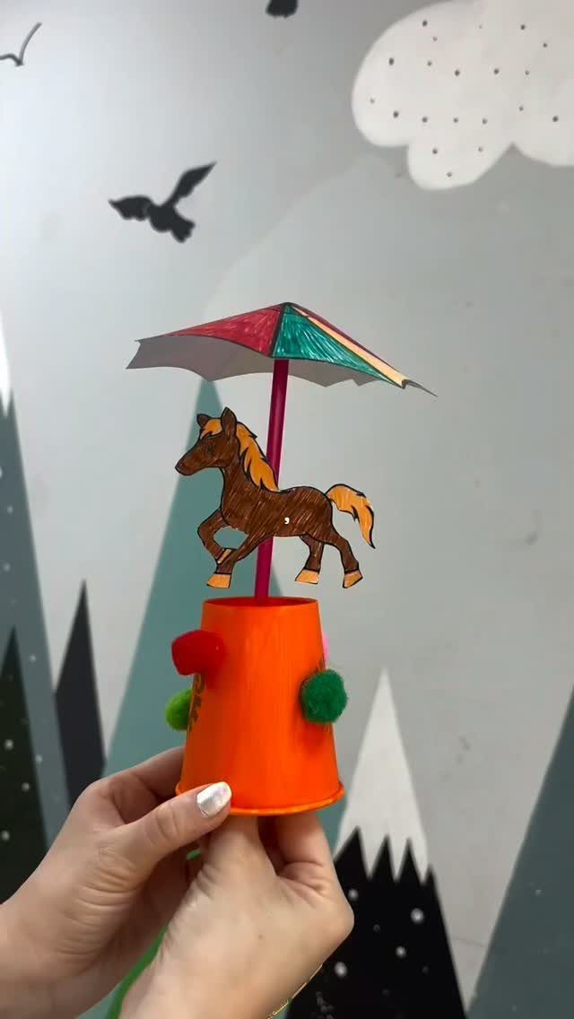 Paper cup horse craft with a colorful umbrella held by two hands.