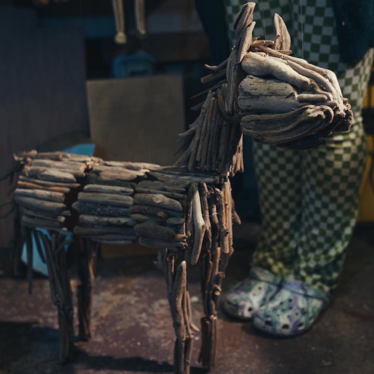 Driftwood horse sculpture standing on a floor next to a person's legs.