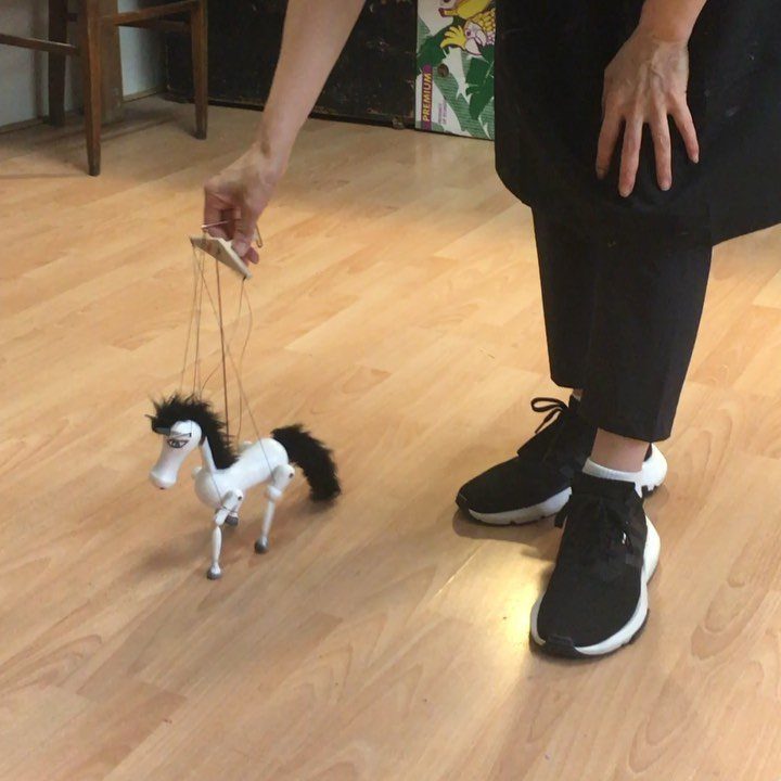 White horse marionette puppet being held by a person on wooden floor