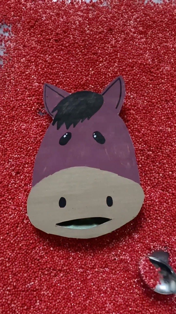 Purple paper horse head resting on a bed of small red sensory beads
