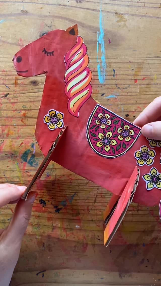 Red cardboard horse craft with colorful floral decorations on a wooden table