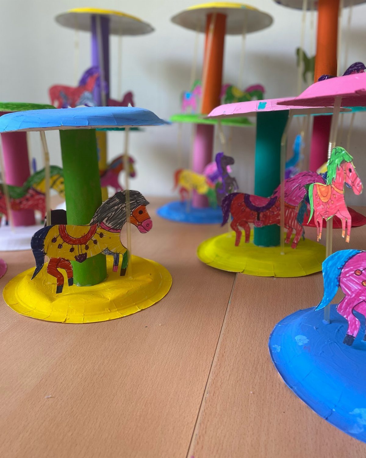 Handmade colorful paper carousels with painted horse figures on a wooden table